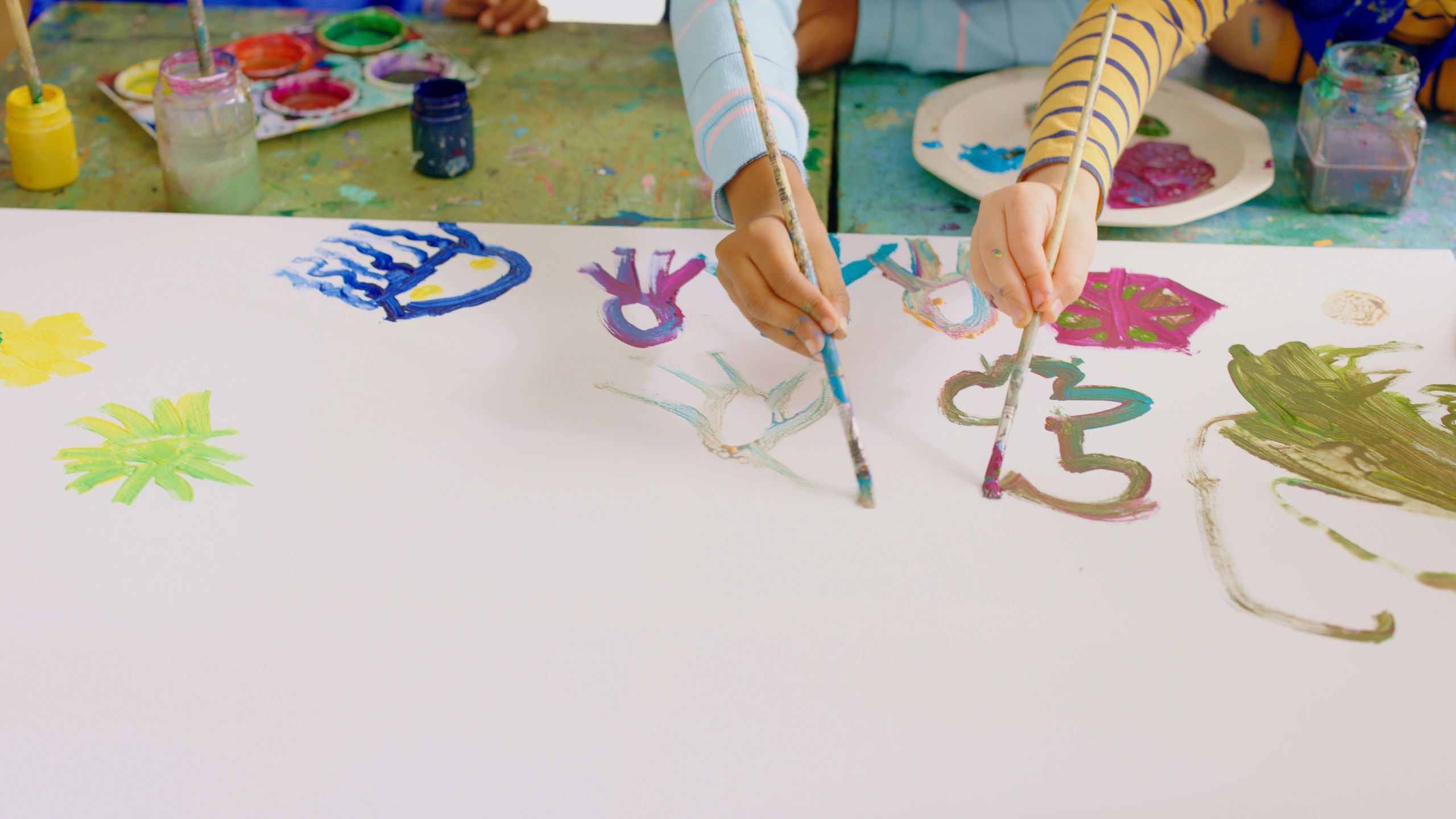 Close-up of children painting with brushes at a classroom table