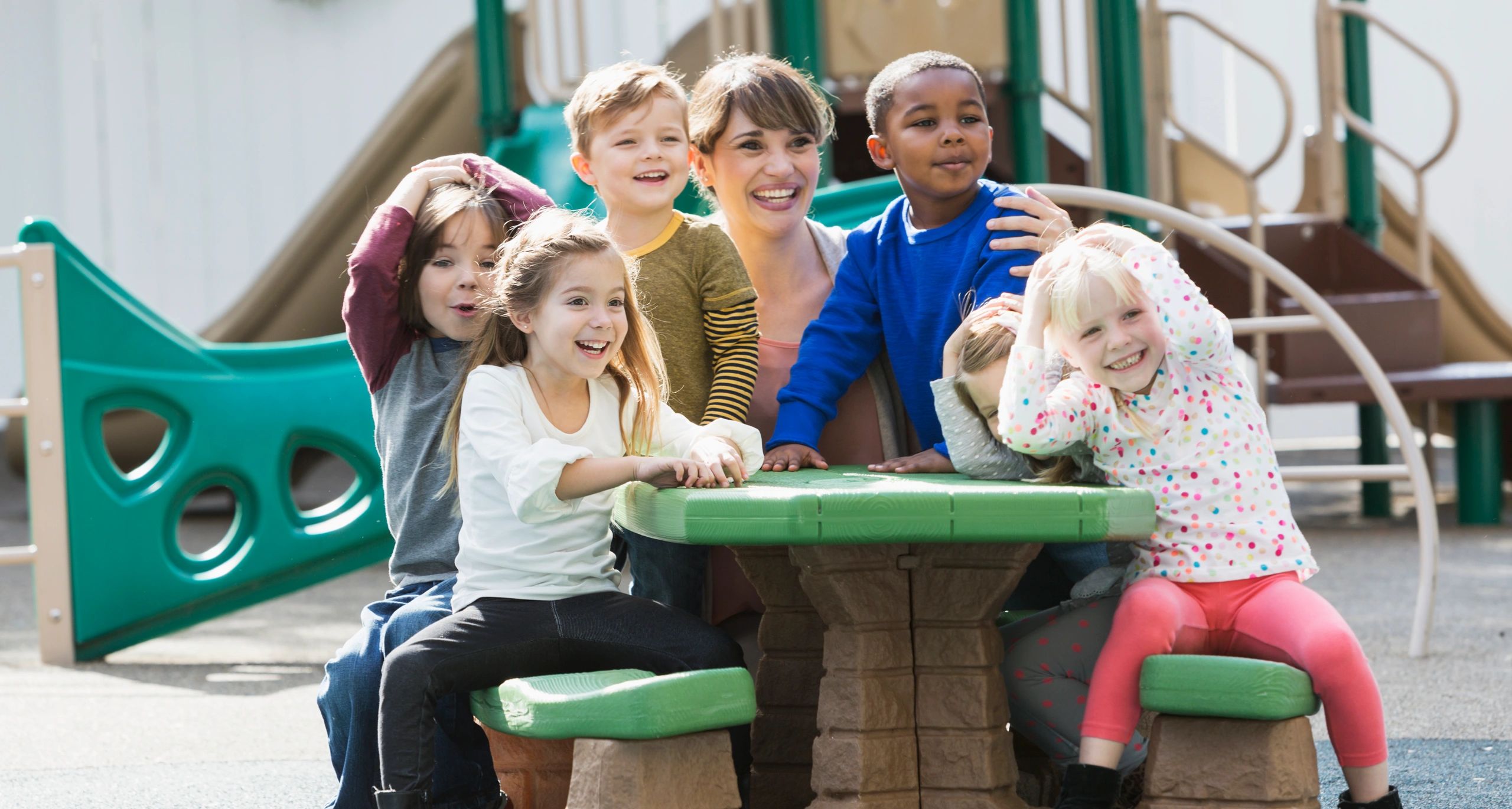Teacher and preschoolers laughing together outdoors